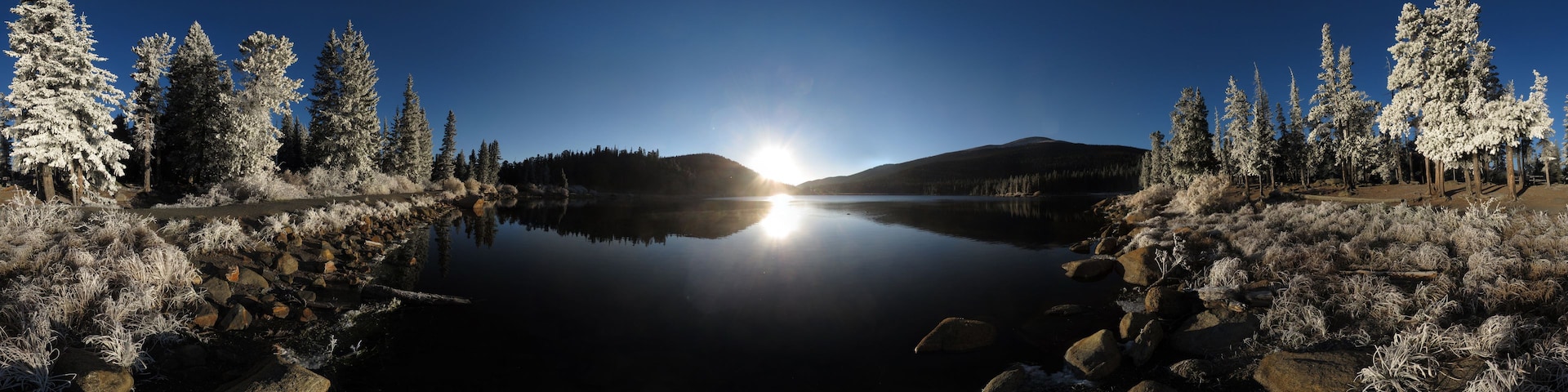 Un lago tranquilo rodeado de árboles y rocas cubiertas de nieve.