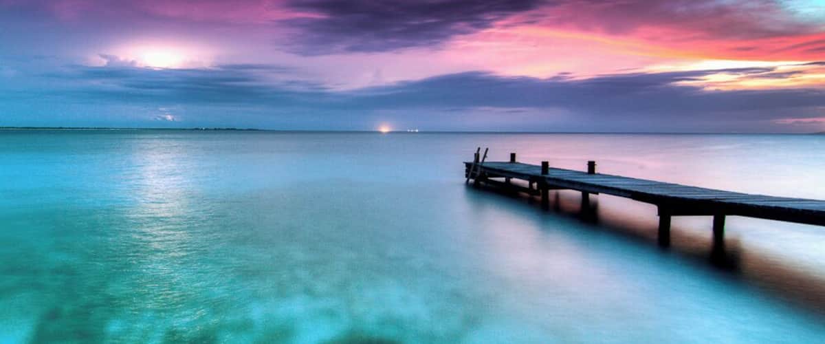 A pier extending into a turquoise sea with a sunset sky.