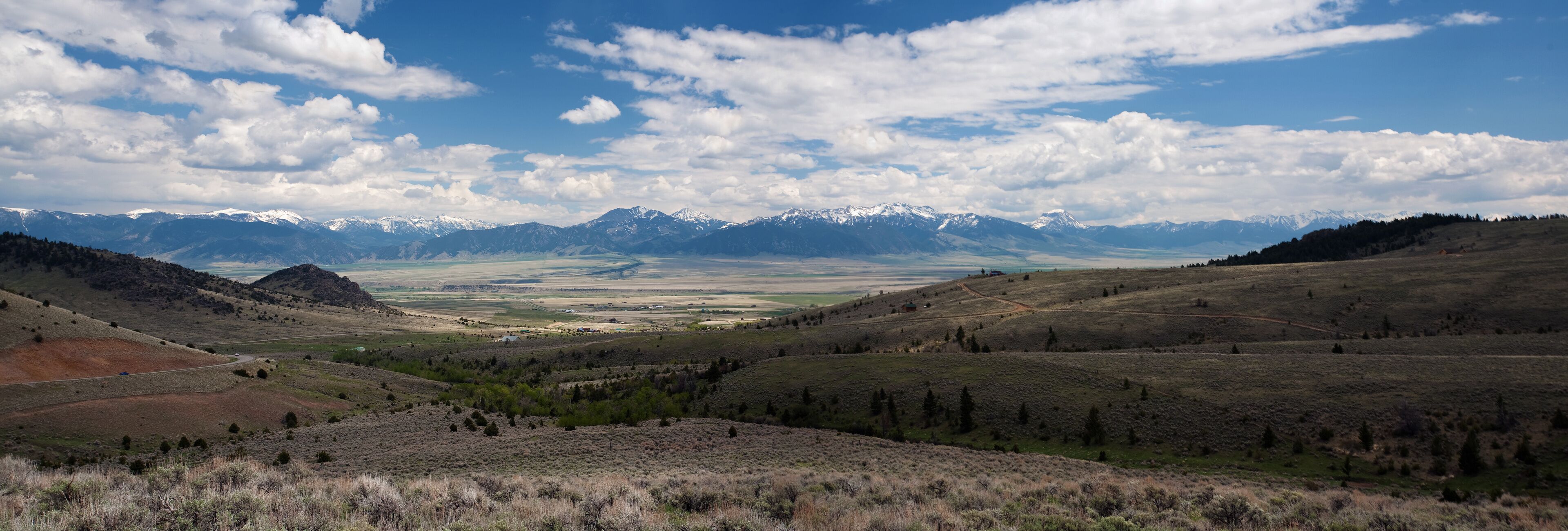 A mountainous landscape with a valley and distant snow-capped peaks.