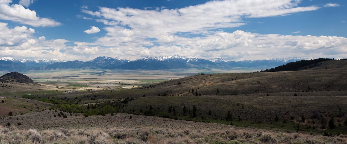 A mountainous landscape with a valley and distant snow-capped peaks.