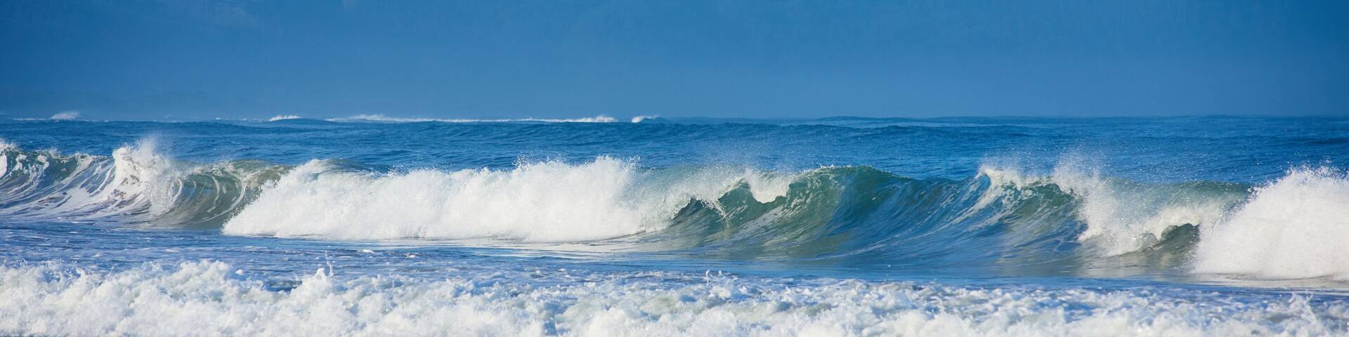 A coastal scene with waves crashing onto the shore and a mountain range in the background.
