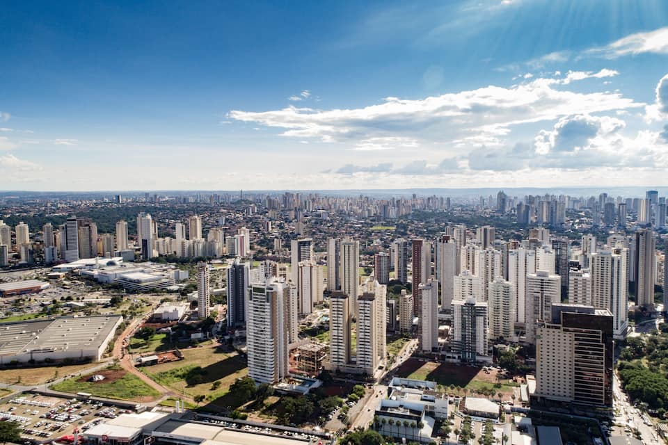 A cityscape with numerous high-rise buildings, a large parking area, and a clear blue sky with scattered clouds.