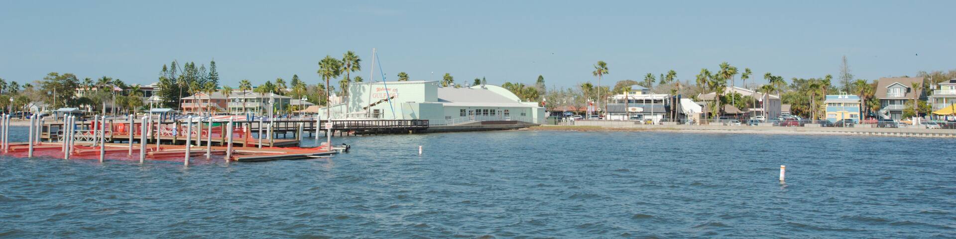 A waterfront with a dock, a boat, and a building with a white roof.