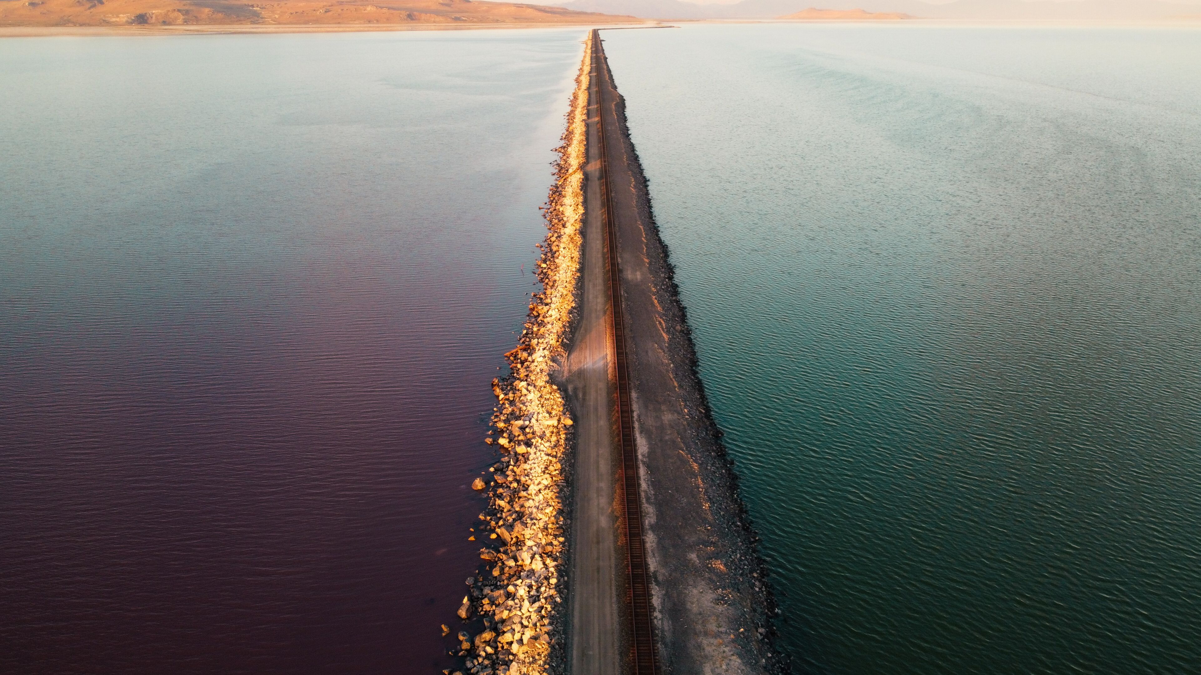 A railway track extending into a body of water with a rocky shoreline.