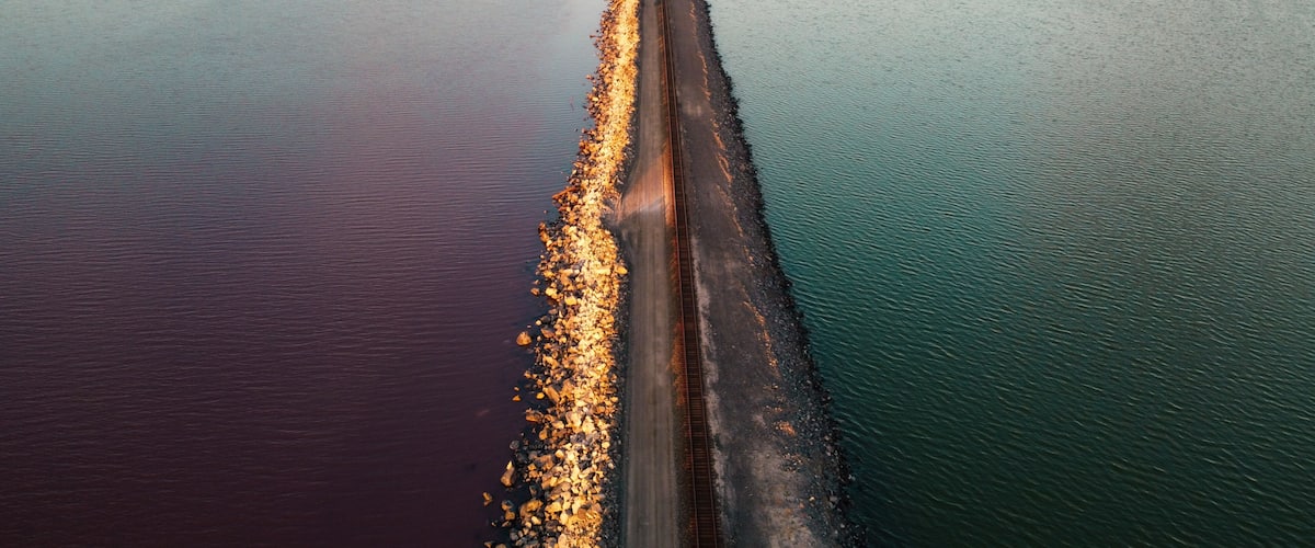 A railway track extending into a body of water with a rocky shoreline.