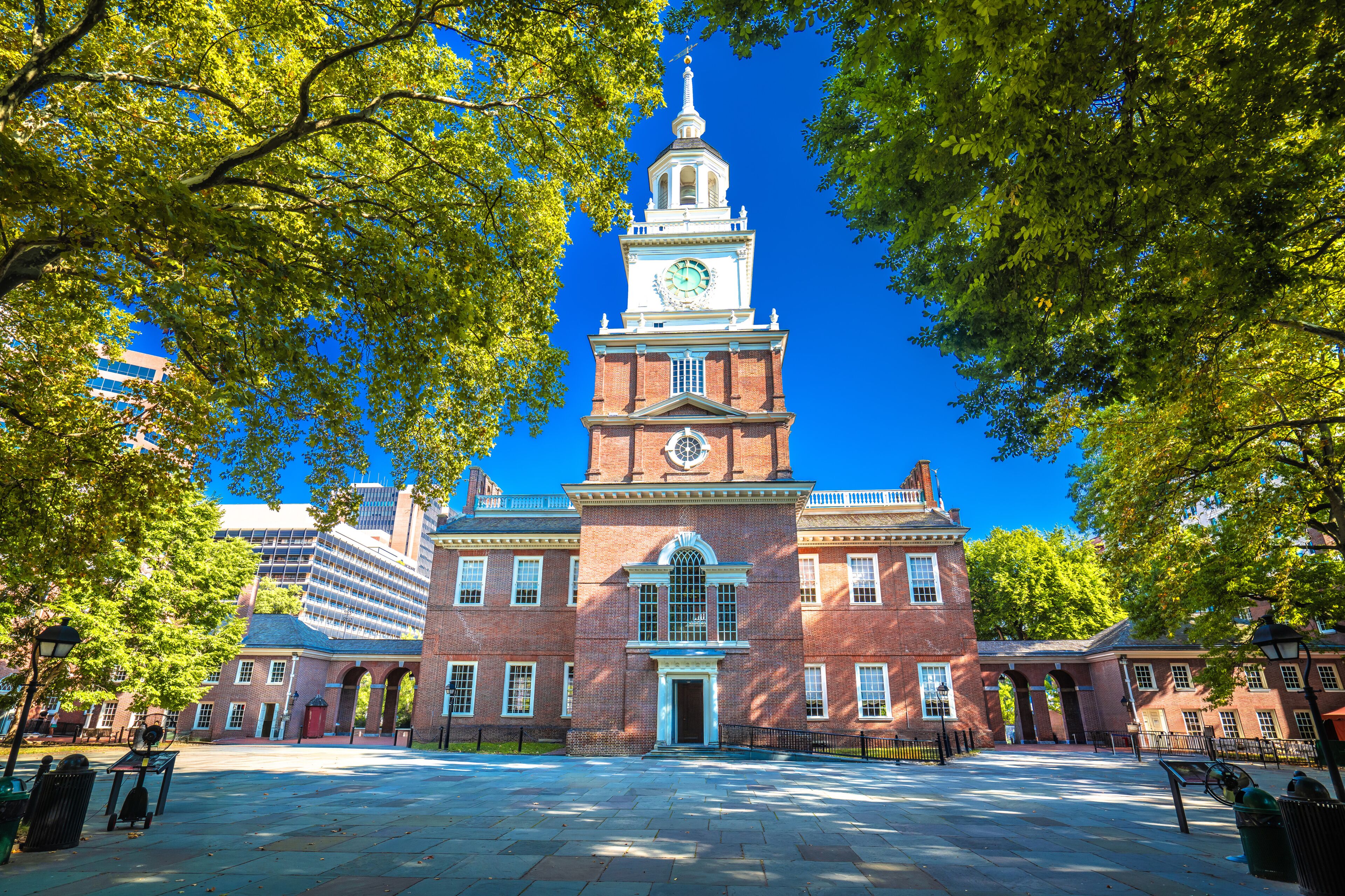 A historic building with a clock tower, surrounded by trees and a paved courtyard.
