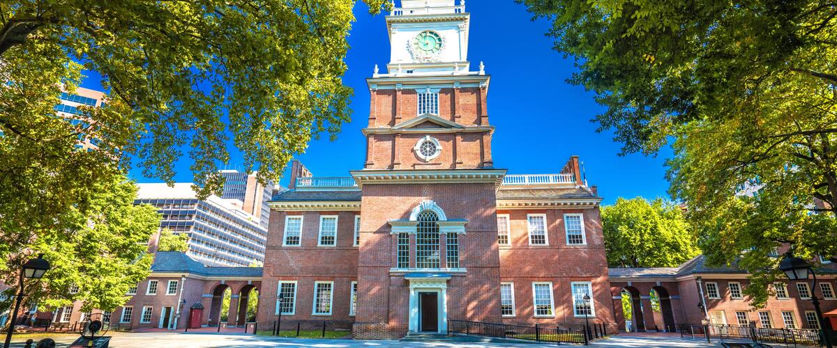 A historic building with a clock tower, surrounded by trees and a paved courtyard.