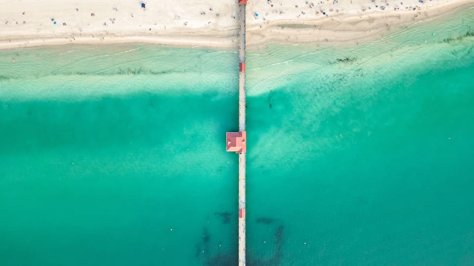 An aerial view of a beach with a pier extending into turquoise waters.