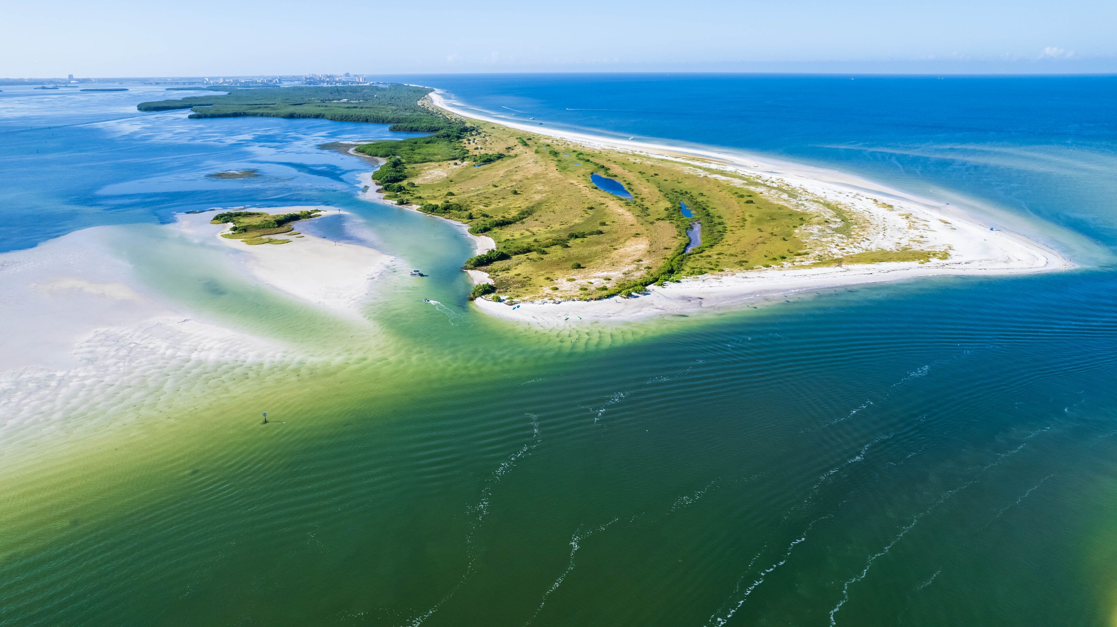 An aerial view of a coastal landscape with a sandy beach, a small island with vegetation, and clear blue waters.
