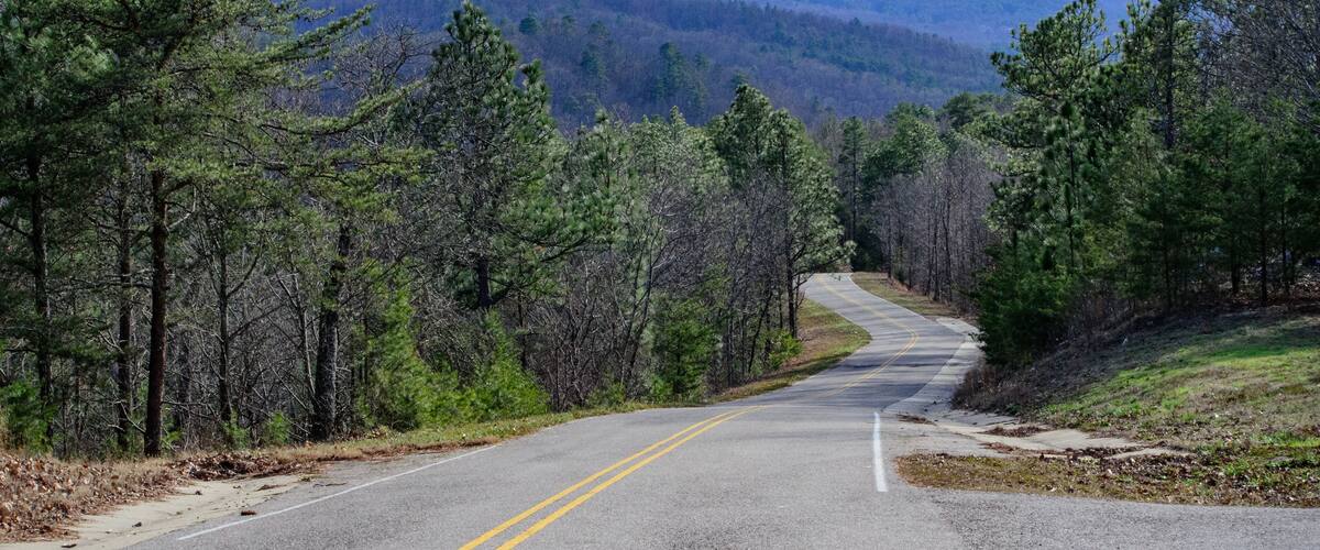 A two-lane road winding through a forested mountain area.