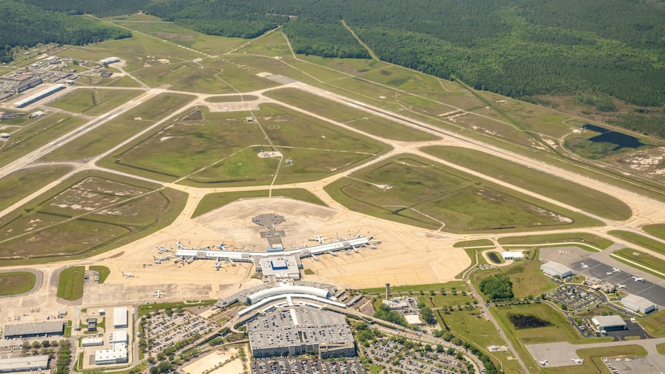An airport with multiple runways, terminal buildings, parking areas, and surrounding green fields.