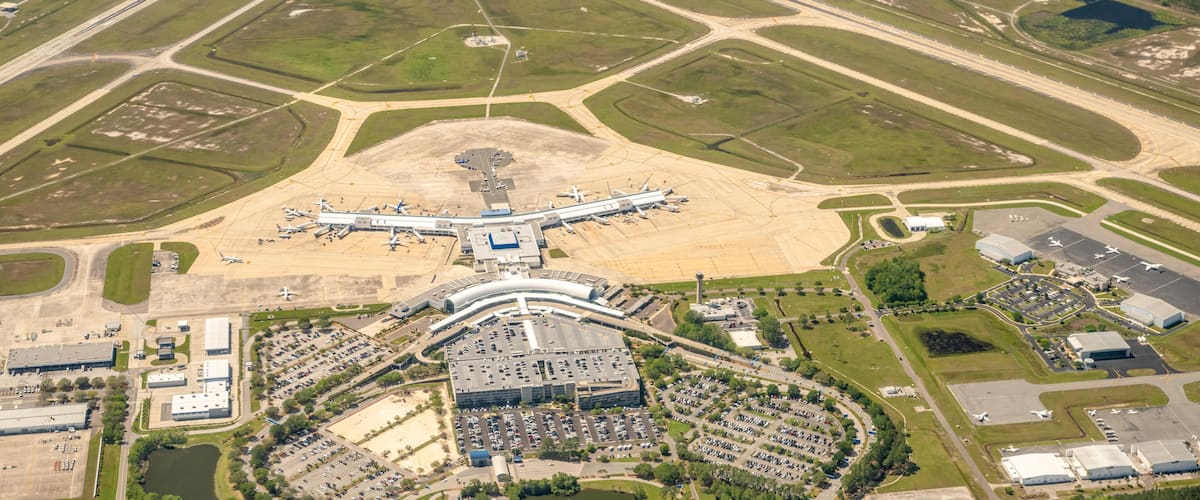 An airport with multiple runways, terminal buildings, parking areas, and surrounding green fields.