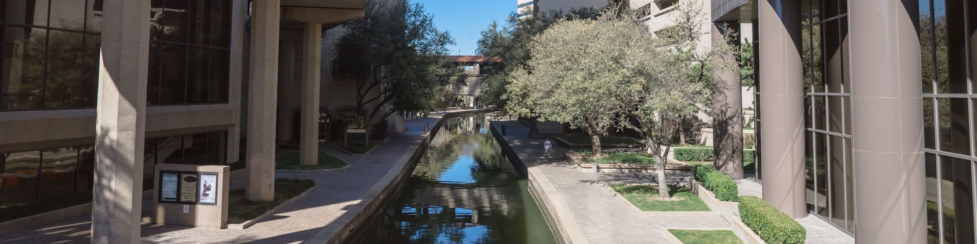 A canal flanked by modern buildings, a clock tower, and a dome structure.