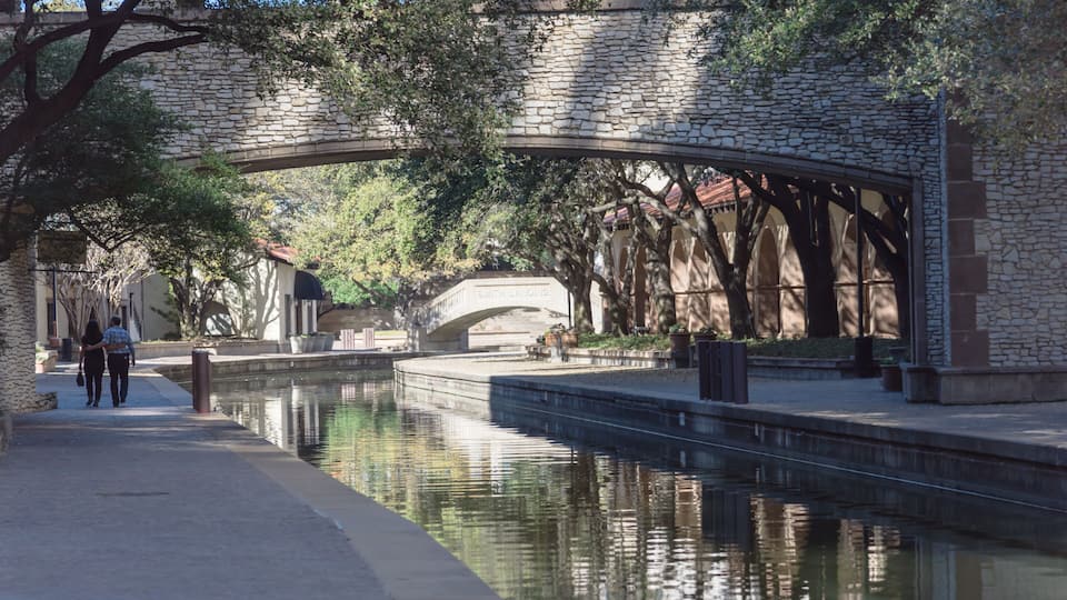 A stone bridge over a canal, surrounded by trees and buildings.