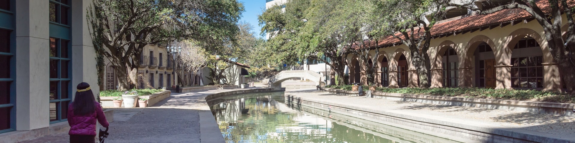Un canal con una persona empujando un cochecito, rodeado de árboles y edificios históricos.