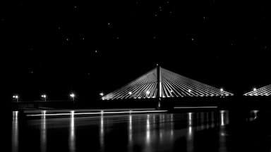 Vista noturna de uma ponte, com seus cabos iluminados sob um céu estrelado.