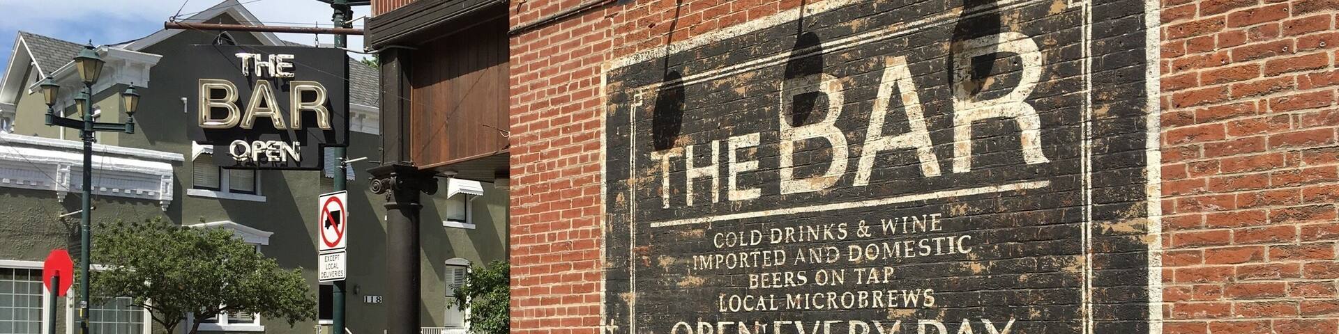 A brick building with a sign that reads "The Bar" and mentions cold drinks, wine, and beers on tap.