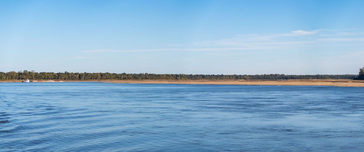 A calm body of water, a sandy beach, and a forested area in the distance.