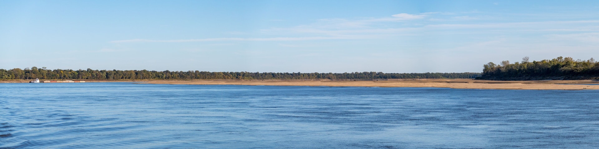 A calm body of water, a sandy beach, and a forested area in the distance.