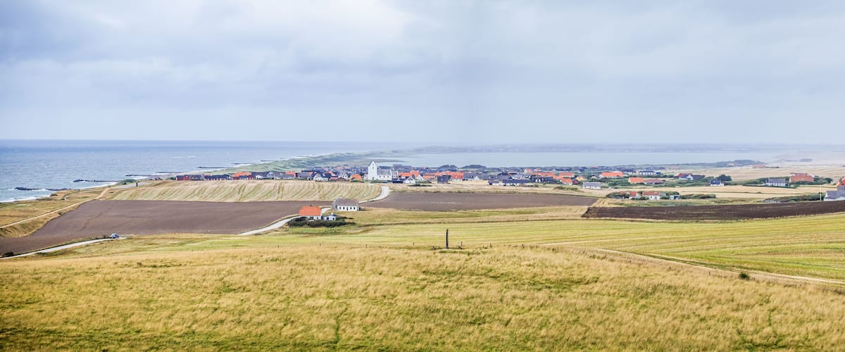 A coastal village with fields, a church, and a road leading to the sea.