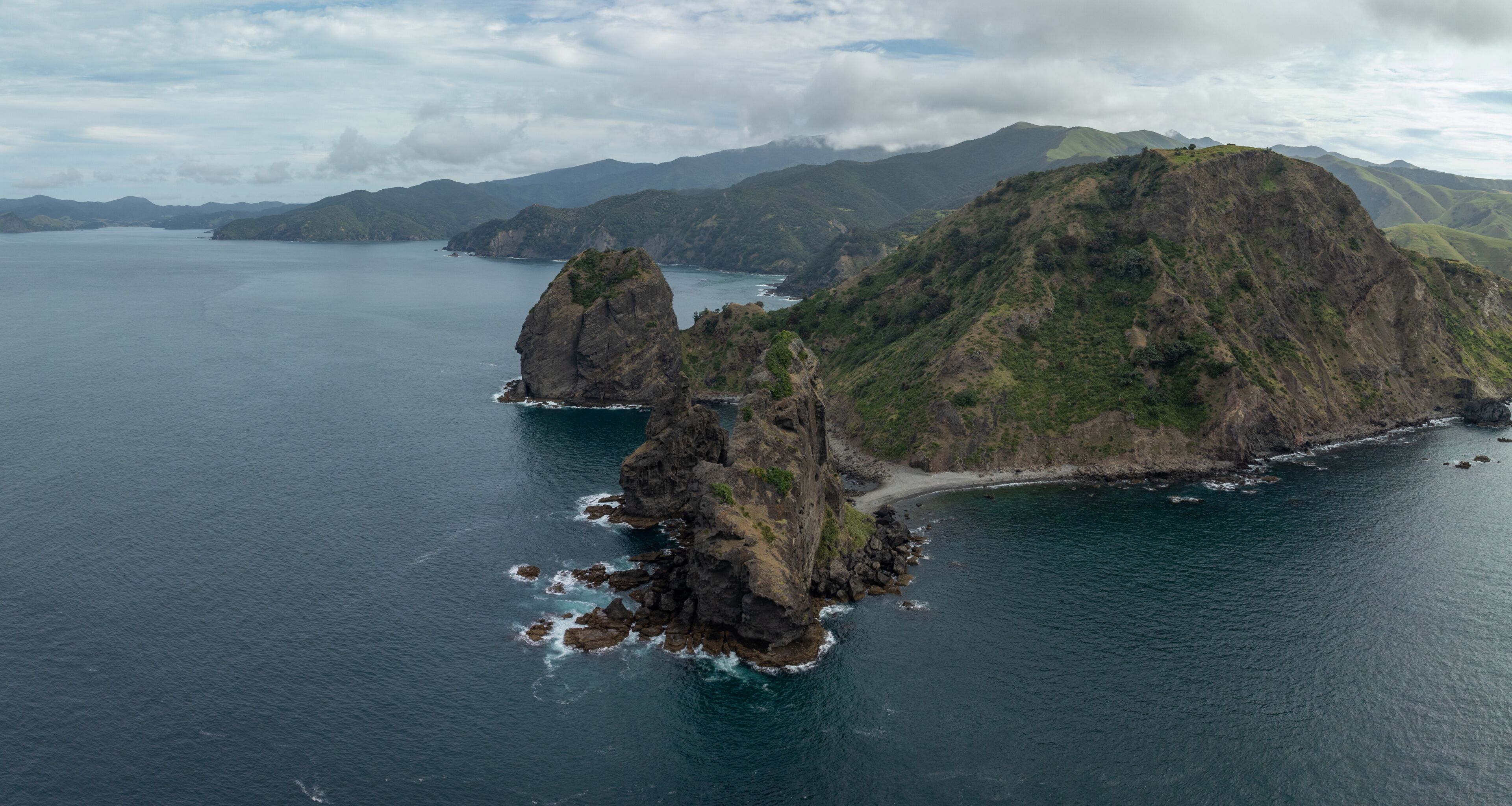 A coastal landscape with rugged cliffs, a small beach, and a large body of water.
