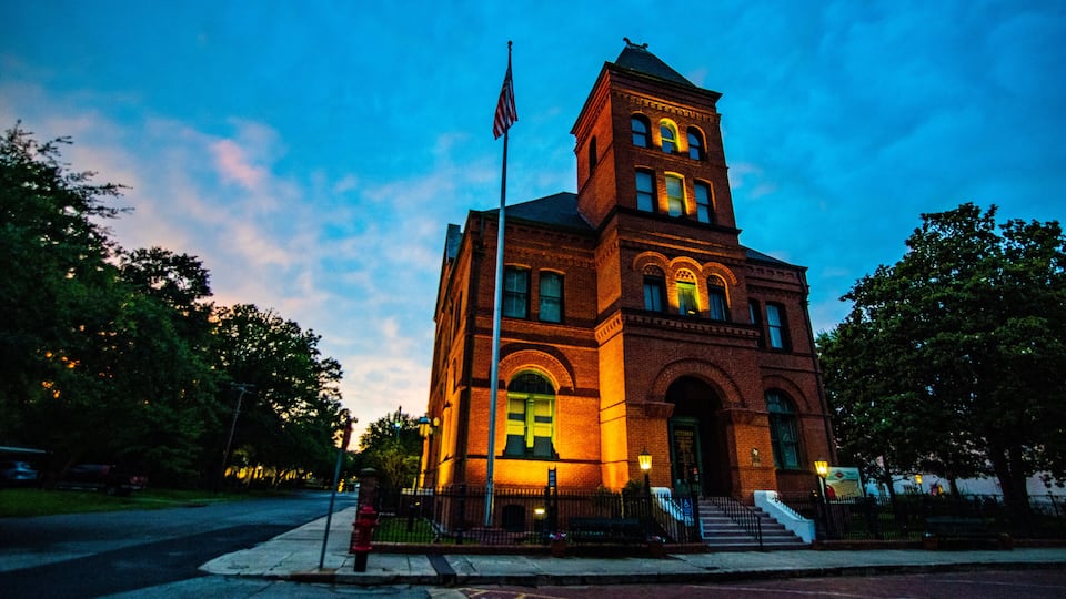 A brick building with a clock tower, a flagpole with an American flag, and a street with a fire hydrant.