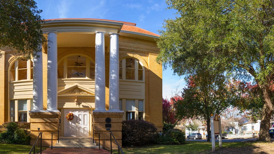 A classical building with columns, a red roof, and a front door with a wreath.