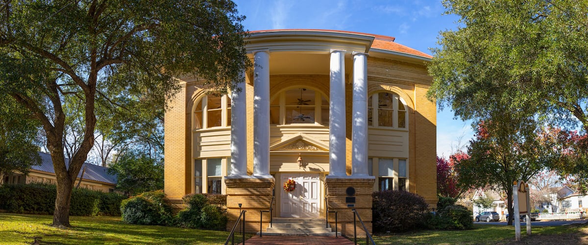 A classical building with columns, a red roof, and a front door with a wreath.
