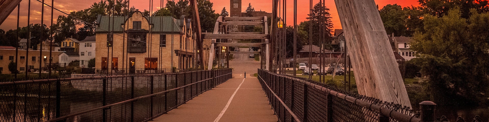 A bridge with a metal framework and a walkway, set against a sunset sky.