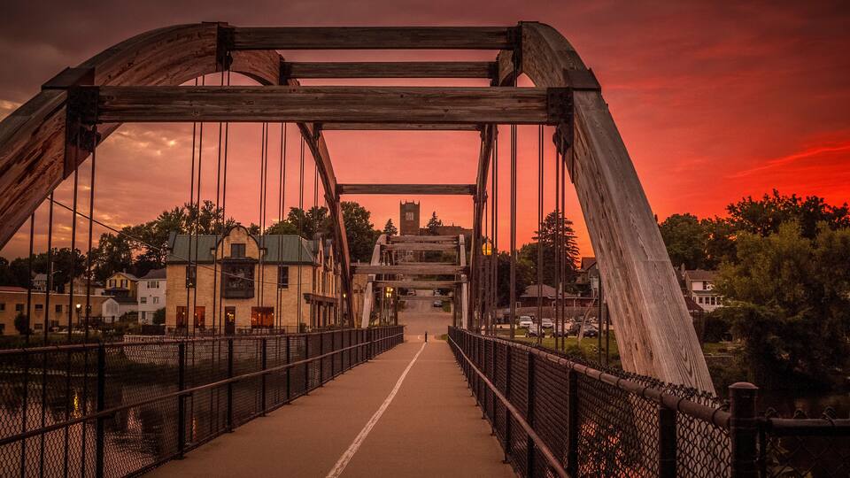 A bridge with a metal framework and a walkway, set against a sunset sky.