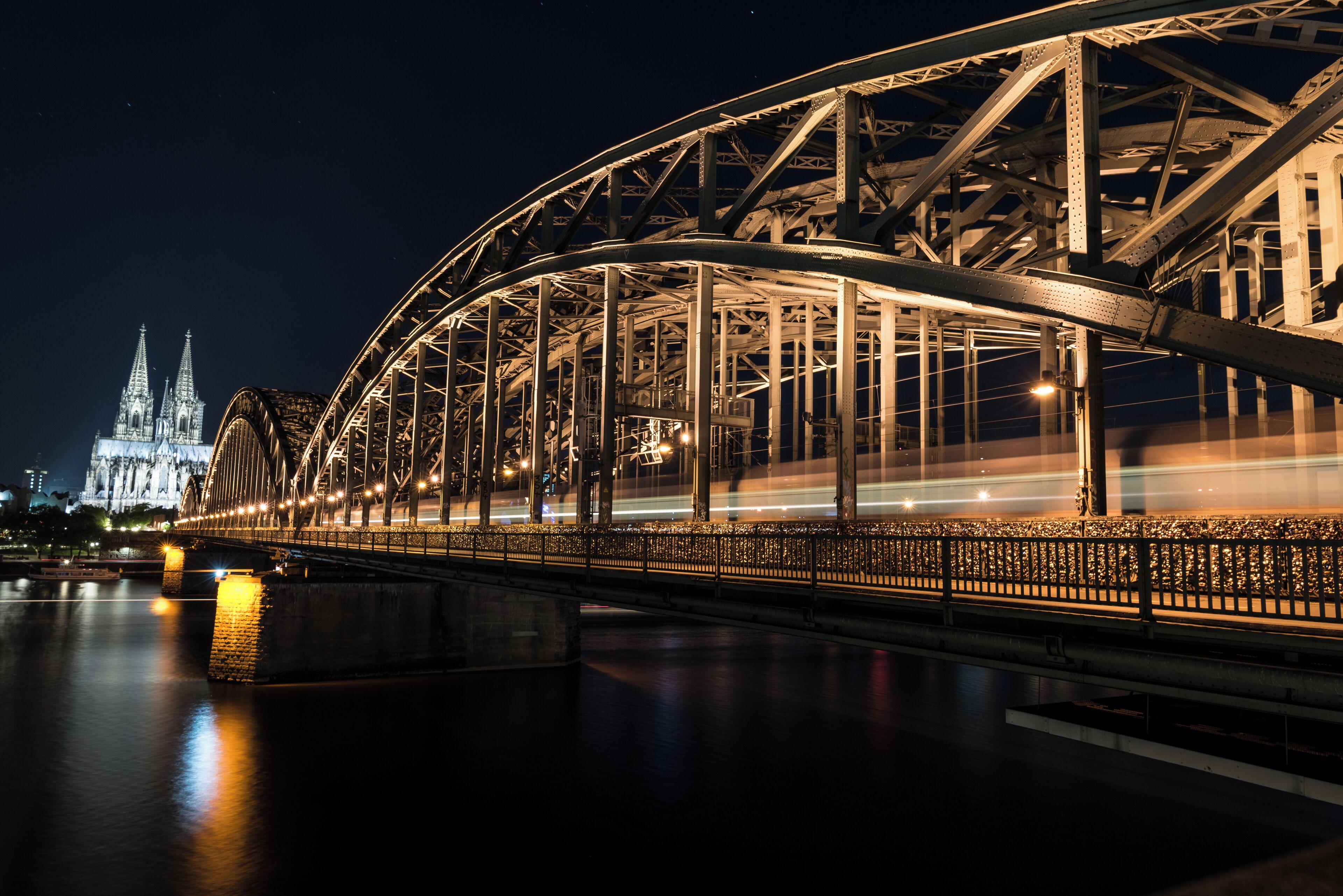 A nighttime view of a steel bridge with a cathedral in the background.