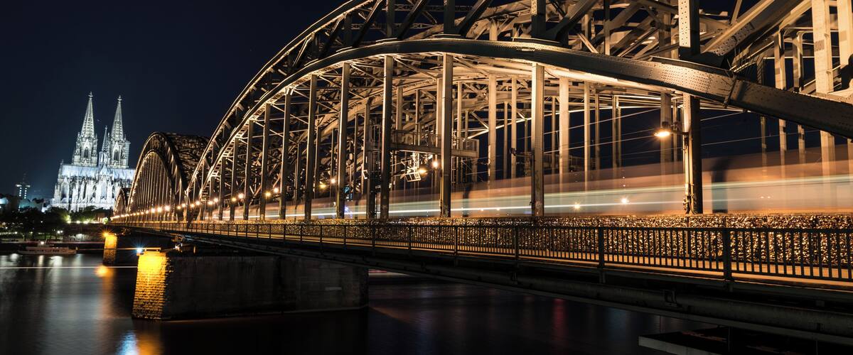 A nighttime view of a steel bridge with a cathedral in the background.