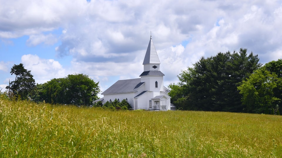 A white church with a steeple in a grassy field.