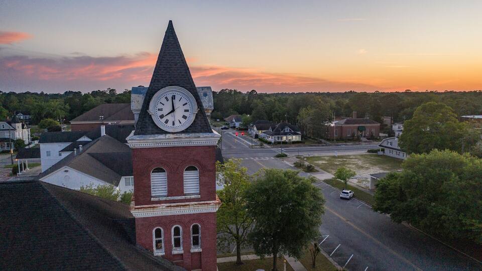 A clock tower, a church, and a street with cars and houses.