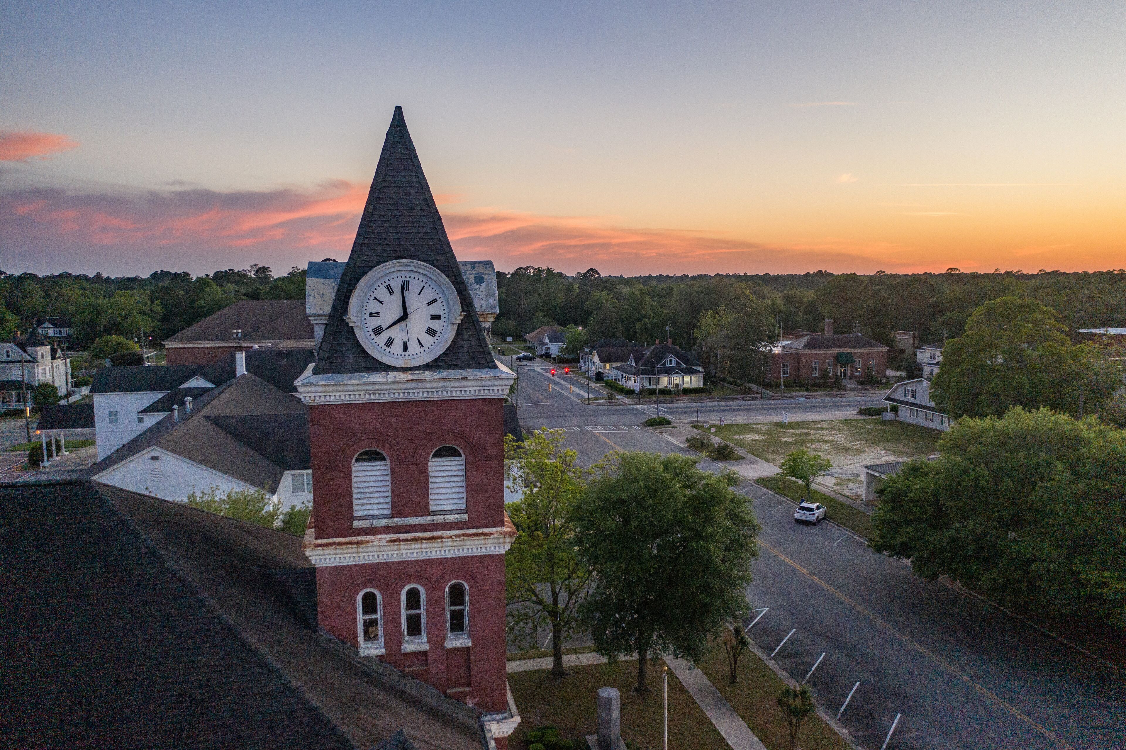 A clock tower, a church, and a street with cars and houses.