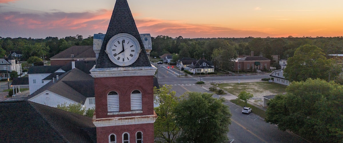 A clock tower, a church, and a street with cars and houses.