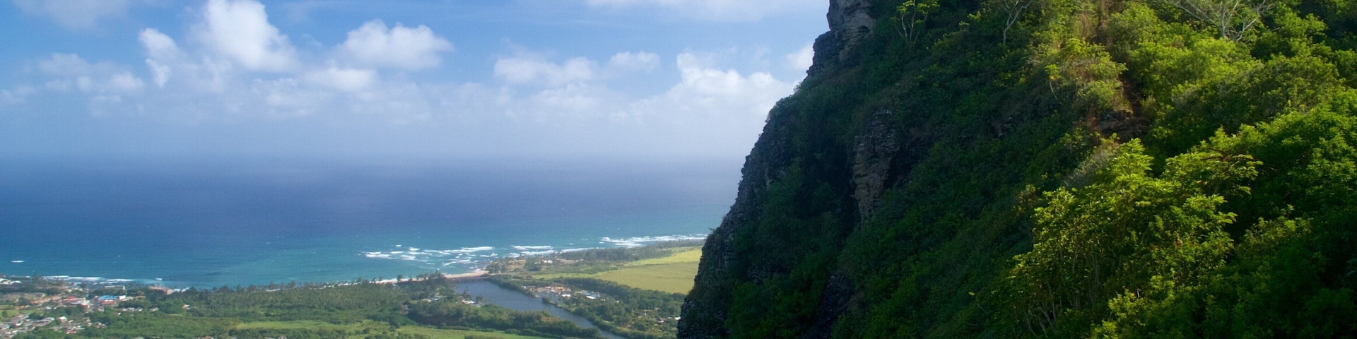 A coastal town nestled between lush green hills and a steep cliff overlooking the ocean.