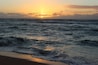 A sunset over the ocean with waves crashing onto the shore.