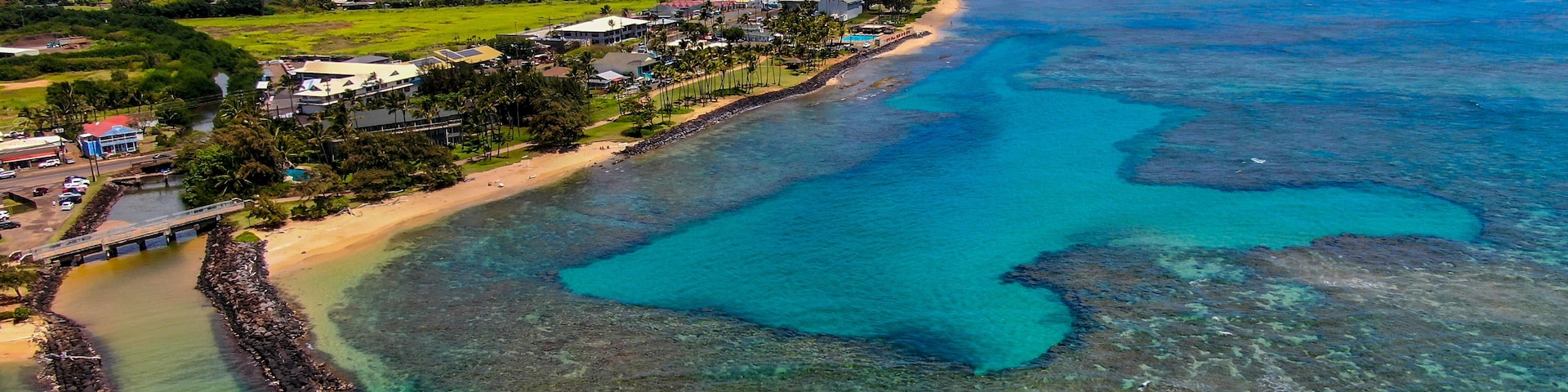 Un pueblo costero con aguas turquesas cristalinas, una playa arenosa y montañas al fondo.