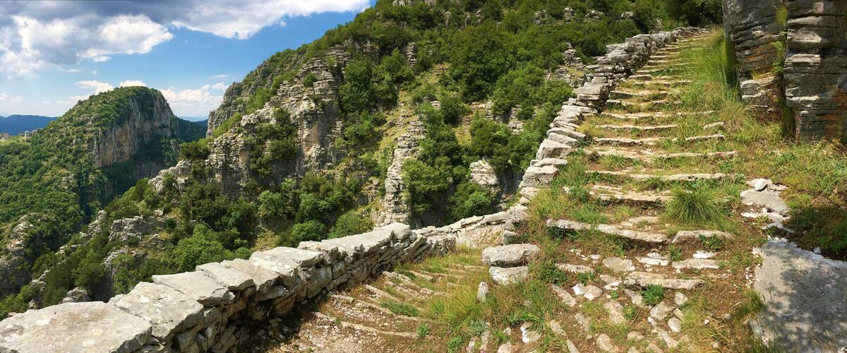 A stone staircase ascending a steep, rocky hillside with lush greenery.