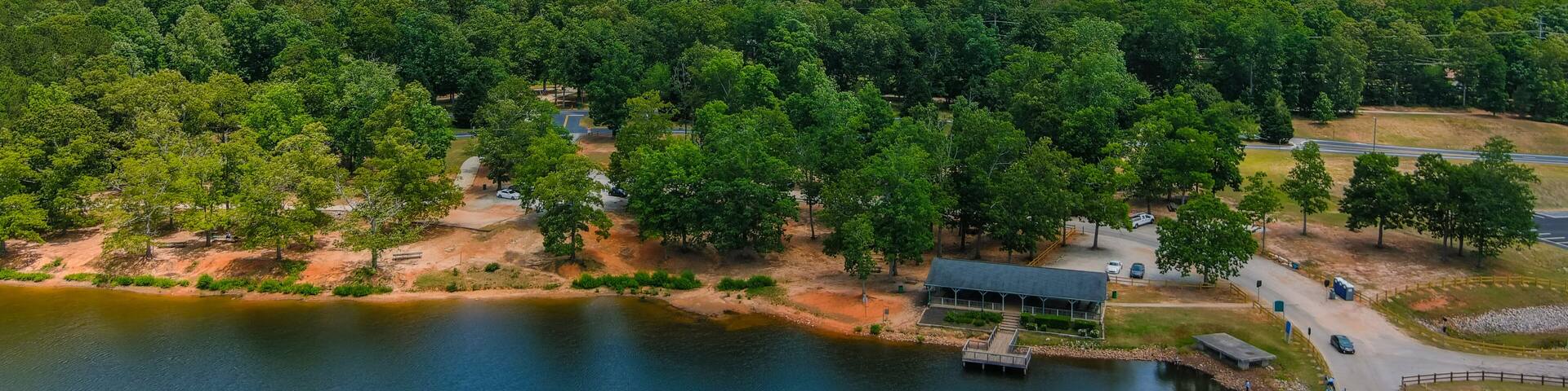 a gorgeous green rippling lake surrounded by lush green trees, grass and plants with blue sky and clouds and buildings among the trees with blue sky and clouds at Lake Spivey Recreation Center