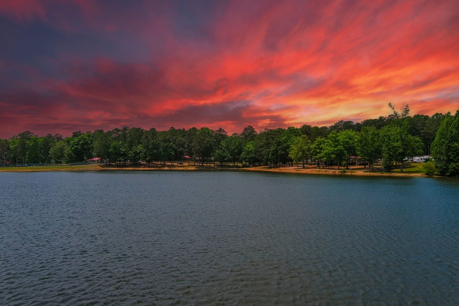 A lake with a sunset sky, trees, and a sandy shore.