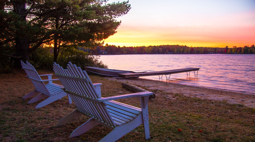 Eine Seenlandschaft mit Adirondack-Stühlen und einem Steg, der ins Wasser ragt.
