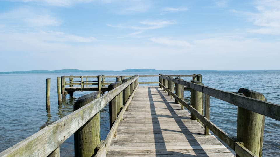 A wooden pier extending into calm water with a clear sky above.