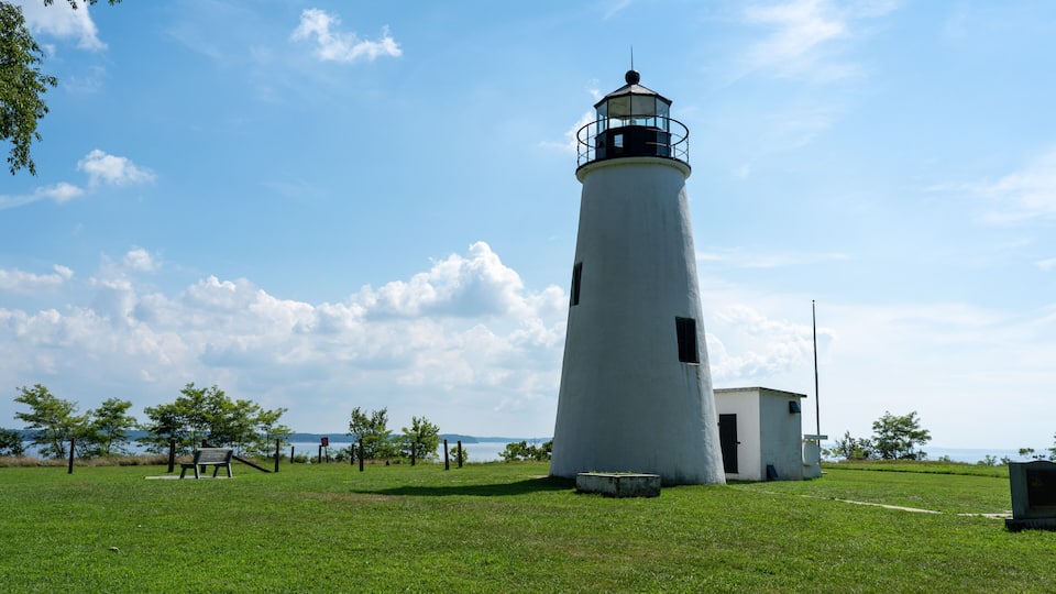 A white lighthouse with a black top, surrounded by a grassy field and a few trees.