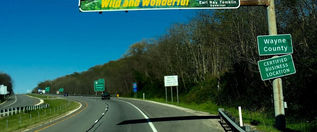 A highway with a welcome sign for West Virginia, a sign for Wayne County, and a certified business location sign.
