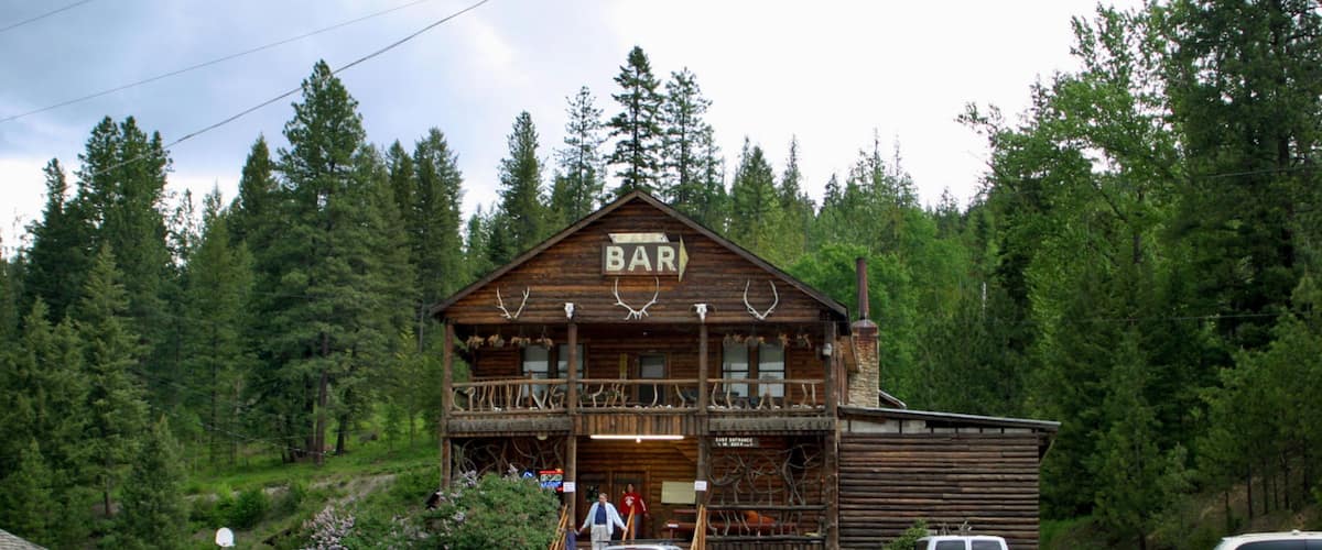 A rustic wooden building labeled 'BAR' with a balcony, surrounded by dense forest.