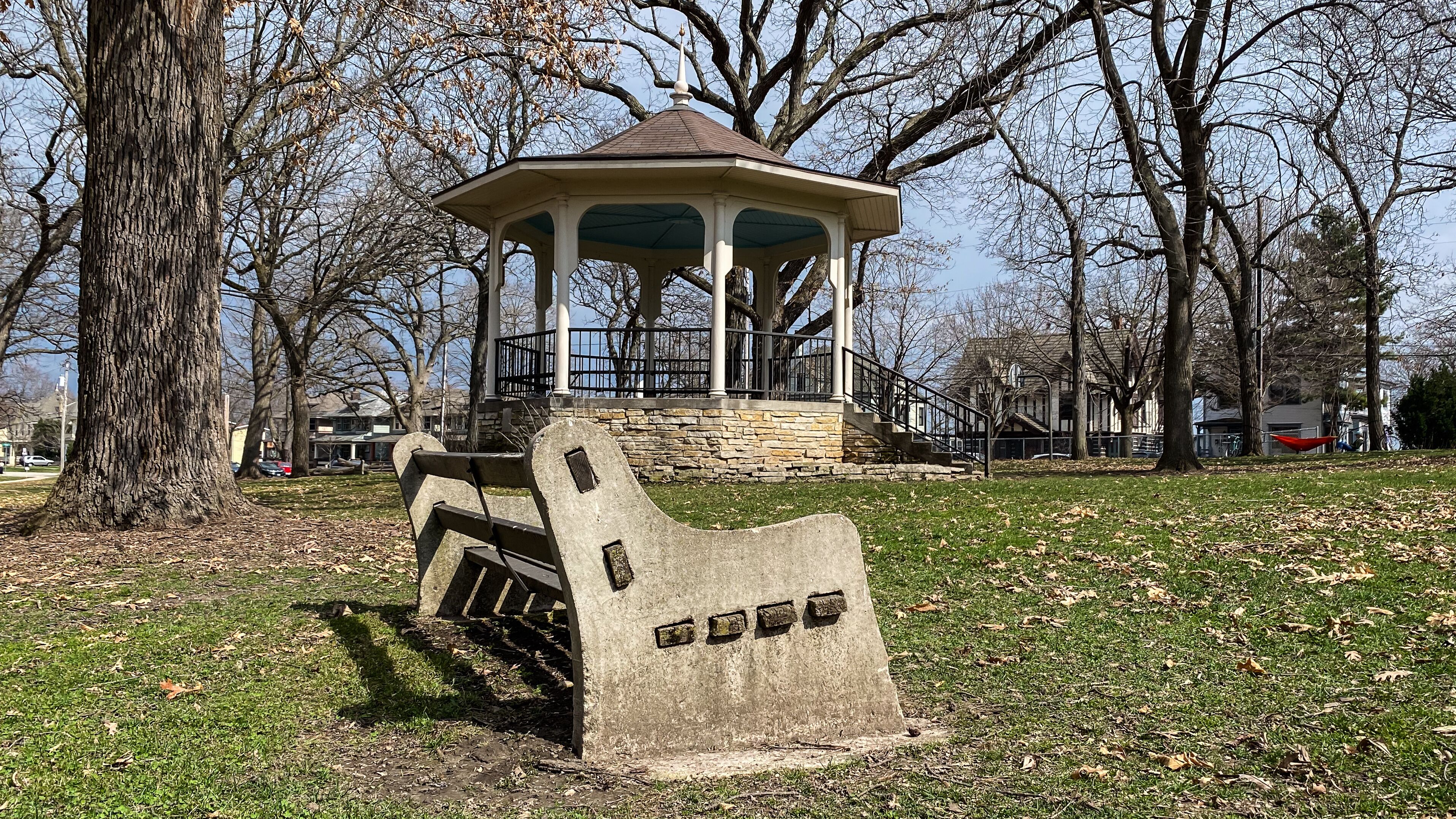 A gazebo in a park with a stone bench in the foreground.
