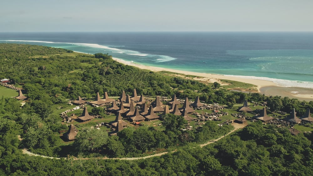 Traditional rural houses at Kodi village, Sumba Island, Indonesia. Aerial view of tropic countryside with buildings landmark at sea bay coast. Cinematic drone shot of summer vacation