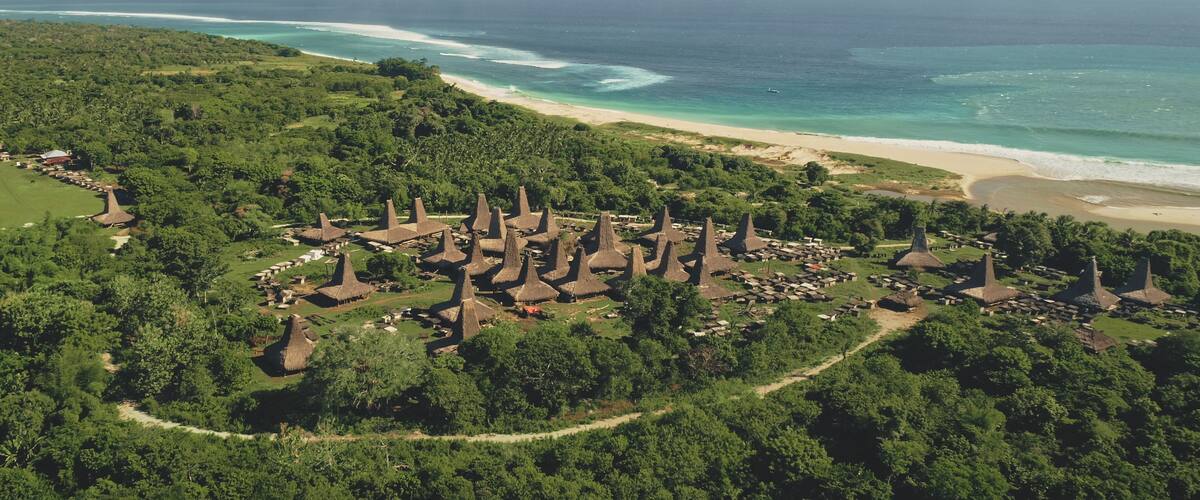 An aerial view of a coastal village with thatched-roof houses and a beach.